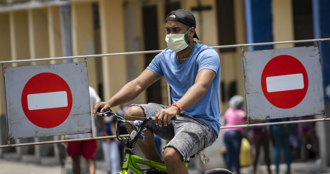 Un hombre con una mascarilla para evitar el contagio del nuevo coronavirus cruza en bicicleta los letreros que prohíben la entrada de vehículos en una zona donde ha aumentado el número de personas infectadas con COVID-19 en el centro de La Habana, Cuba, el sábado 9 de mayo de 2020.