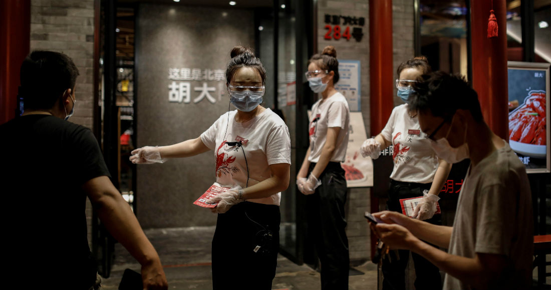 Camareras con máscaras de protección, guantes y gafas dan la bienvenida a las personas que entran en un restaurante en medio de la pandemia de coronavirus después de que se detectaran nuevos de COVID-19 en Pekín, China.