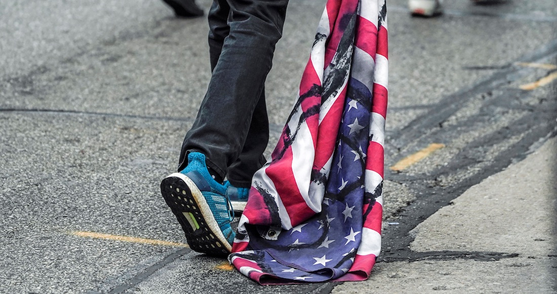 Un manifestante arrastra una bandera de los Estados Unidos durante una protesta después de la visita del Presidente Donald Trump en Wisconsin.