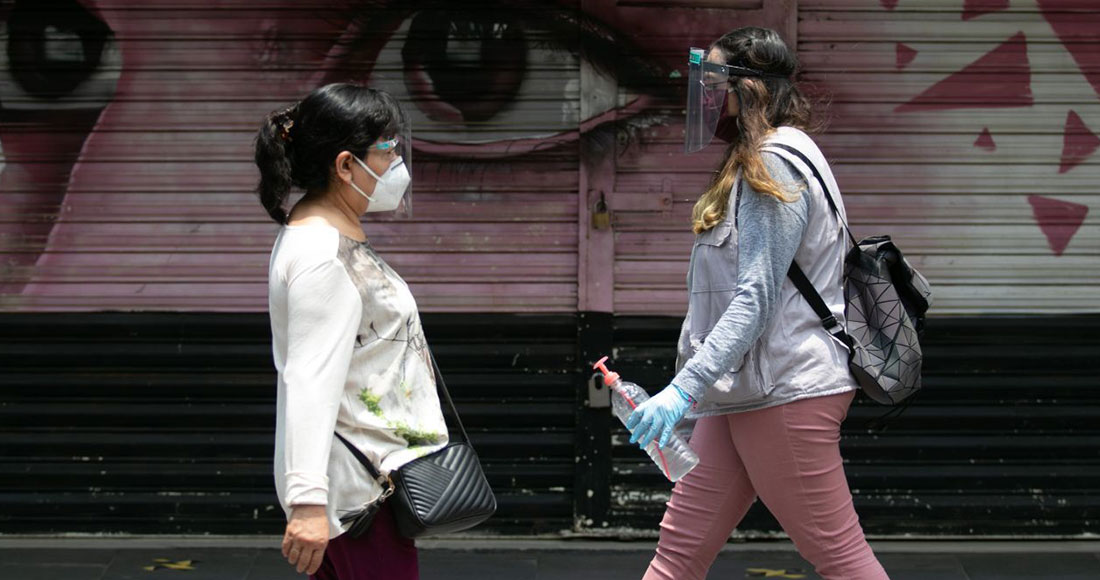 Dos mujeres portando careta pasan frente al mural en la reja de un local del Centro Histórico en la Ciudad de México. Foto: Galo Cañas, Cuartoscuro