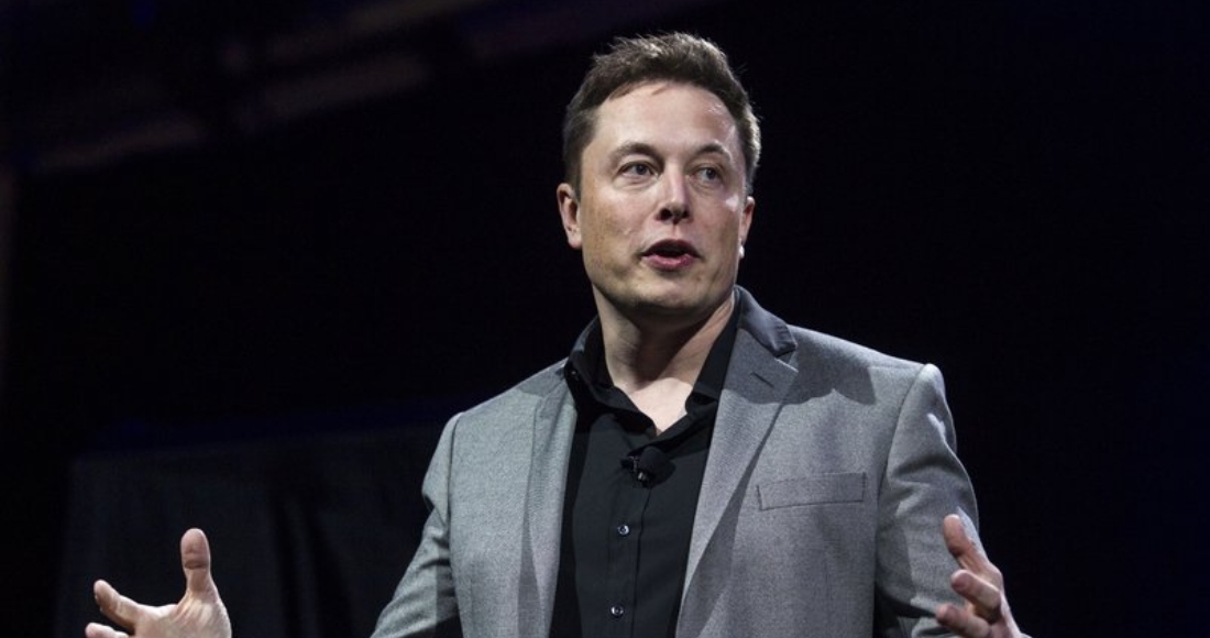 elon-musk-traje-gris-camisa-negra-manos-abiertas