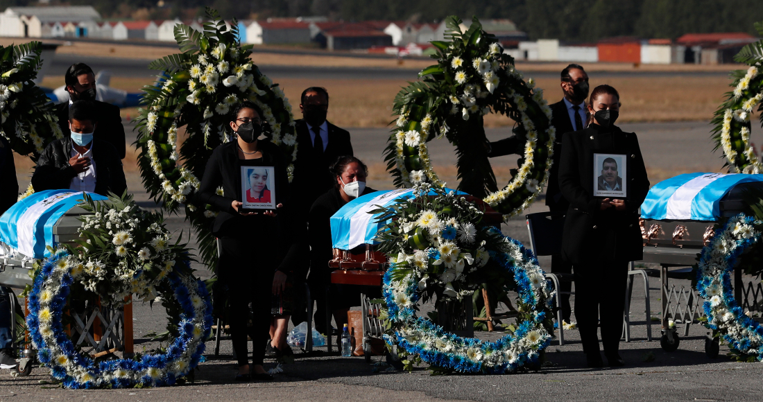 La gente espera de pie con fotografías mientras los restos de 16 migrantes guatemaltecos que fueron asesinados cerca de la frontera entre Estados Unidos y México en enero llegan a la base de la Fuerza Aérea en la Ciudad de Guatemala, el viernes 12 de marzo de 2021.